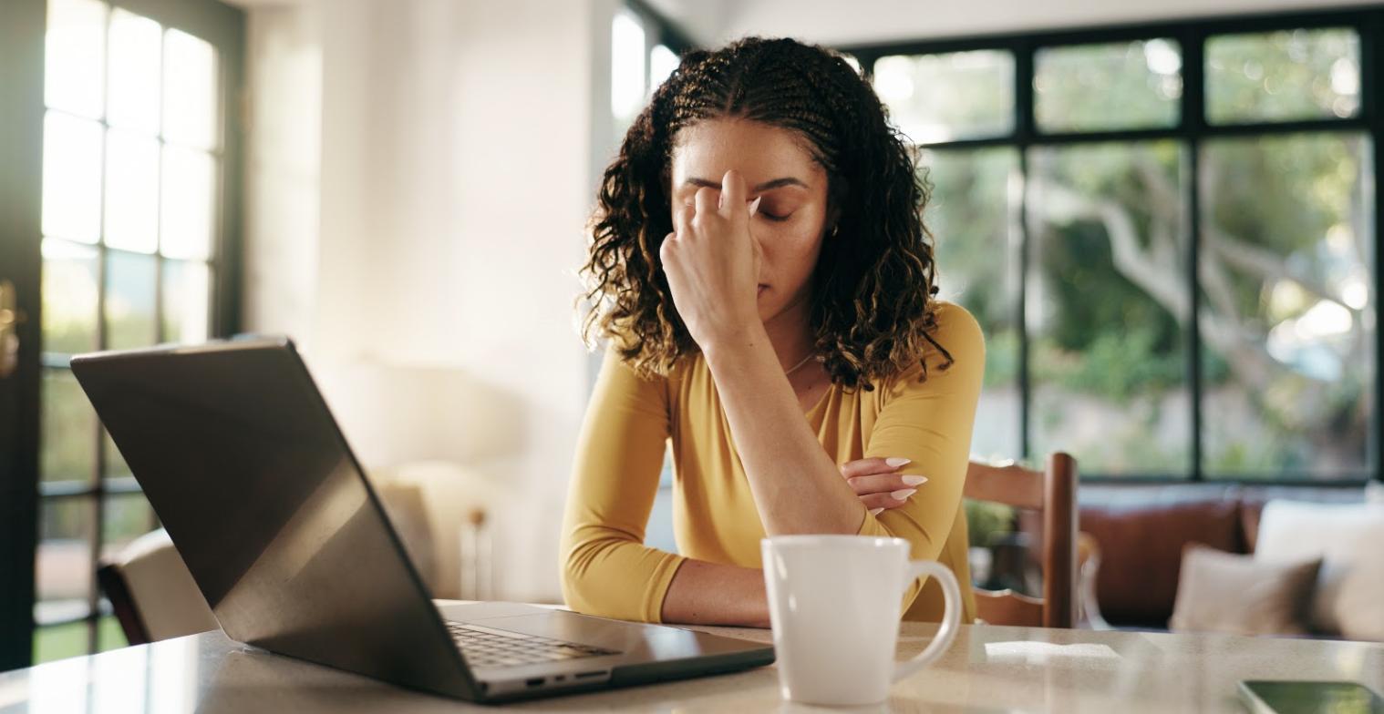 A woman at her laptop presses her fingers to her brow, the experience of a medication that is not working as expected