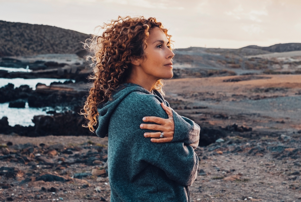 Woman standing in open countryside at dusk, arms wrapped around herself