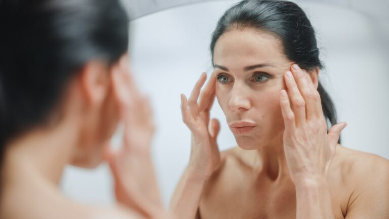 Woman in midlife examining her skin in a mirror, illustrating what GHK-Cu copper peptide does for menopause skin