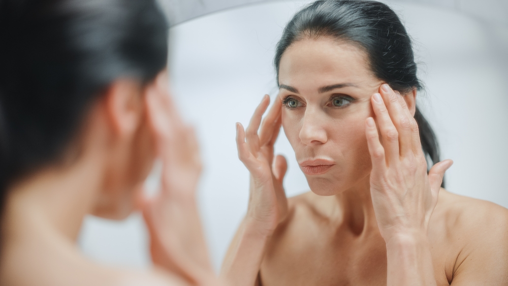Woman in midlife examining her skin in a mirror, illustrating what GHK-Cu copper peptide does for menopause skin