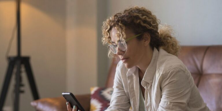 Woman in midlife at home logging her perimenopause symptoms on her phone in the Harmoni app