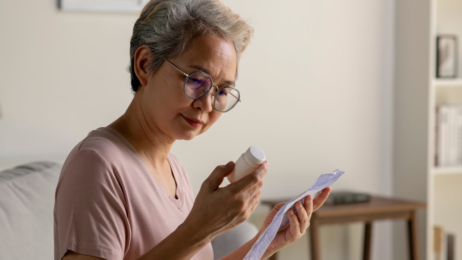 Asian woman in her 50s with glasses reading the information sheet for her hormone replacement therapy prescription at home