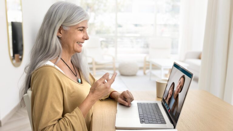Latina woman in her 50s with silver hair smiling during a telehealth video visit about testosterone therapy on her laptop at home in Arizona